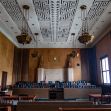 A courtroom with wooden benches and a decorative ceiling, depicting a formal setting for legal proceedings. A courtroom with wooden benches and a decorative ceiling, depicting a formal setting for legal proceedings.
