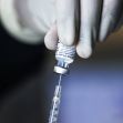 A gloved hand holding a vial of COVID-19 vaccine while preparing a syringe for vaccination. A gloved hand holding a vial of COVID-19 vaccine while preparing a syringe for vaccination.