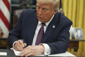 Trump signing a document in the Oval Office.