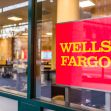 Wells Fargo bank sign displayed at a branch location, with the interior visible through the glass window. Wells Fargo bank sign displayed at a branch location, with the interior visible through the glass window.