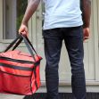A delivery worker holding a red insulated food delivery bag standing at a residential doorway. A delivery worker holding a red insulated food delivery bag standing at a residential doorway.