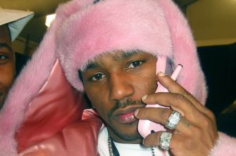 Cam’ron wearing a fuzzy pink coat and hat, holding a pink flip phone.