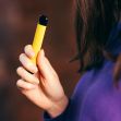 A person holding a yellow e-cigarette device. A person holding a yellow e-cigarette device.