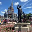 A statue of Walt Disney holding hands with Mickey Mouse in front of Cinderella Castle, surrounded by colorful flowers and visitors at a theme park. A statue of Walt Disney holding hands with Mickey Mouse in front of Cinderella Castle, surrounded by colorful flowers and visitors at a theme park.