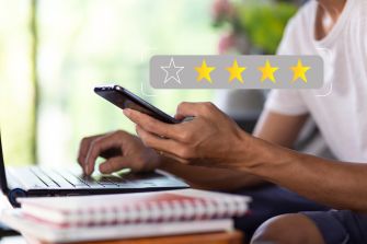 A person using a smartphone while sitting at a desk with a laptop and notebooks, indicating engagement with social media or online comments.