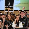 A group of actors and union representatives at a press conference, all showing solidarity with raised fists and holding signs that read "SAG-AFTRA ON STRIKE!" A group of actors and union representatives at a press conference, all showing solidarity with raised fists and holding signs that read "SAG-AFTRA ON STRIKE!"