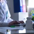 A medical professional working at a desk with a prescription bottle and syringe, highlighting issues related to healthcare practices. A medical professional working at a desk with a prescription bottle and syringe, highlighting issues related to healthcare practices.
