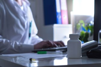 A medical professional working at a desk with a prescription bottle and syringe, highlighting issues related to healthcare practices.