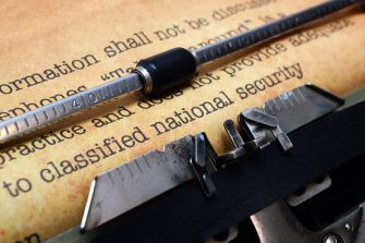 Close-up of a typewriter with a sheet of paper that has text related to classified national security information.