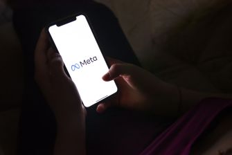 A person holding a smartphone displaying the Meta logo, featuring the infinity symbol.