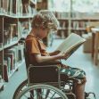 A child in a wheelchair reading a book in a library setting. A child in a wheelchair reading a book in a library setting.