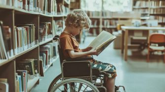 A child in a wheelchair reading a book in a library setting.
