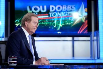Lou Dobbs sitting at the set of "Lou Dobbs Tonight" with a graphic of the show's title in the background.