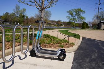 A dock-less electric scooter parked by a bike rack in a public area.