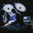 Surgeons performing a medical procedure in an operating room, with bright surgical lights and medical equipment in the background. Surgeons performing a medical procedure in an operating room, with bright surgical lights and medical equipment in the background.