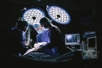 Surgeons performing a medical procedure in an operating room, with bright surgical lights and medical equipment in the background.