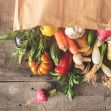 A paper bag spilling over with fresh vegetables and herbs on a wooden surface. A paper bag spilling over with fresh vegetables and herbs on a wooden surface.
