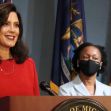 Governor Gretchen Whitmer speaking at a press conference with another official, with flags displayed in the background. Governor Gretchen Whitmer speaking at a press conference with another official, with flags displayed in the background.