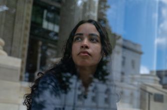 A young woman looking thoughtfully out a window, reflecting on her experiences and challenges in education.