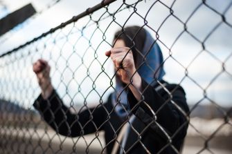 A woman holding onto a chain-link fence, symbolizing the plight of immigrants facing detention.
