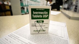 A box of Ivermectin tablets on a pharmacy counter, with prescription paperwork in the background.