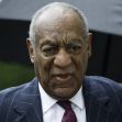 Bill Cosby walking under an umbrella, appearing serious during a legal proceeding. Bill Cosby walking under an umbrella, appearing serious during a legal proceeding.