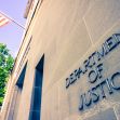 Sign on the exterior of the U.S. Department of Justice building, with an American flag in the background. Sign on the exterior of the U.S. Department of Justice building, with an American flag in the background.