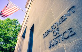 Sign on the exterior of the U.S. Department of Justice building, with an American flag in the background.