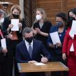California Governor Gavin Newsom signs a new COVID-19 sick leave law, surrounded by officials and supporters, all wearing masks. California Governor Gavin Newsom signs a new COVID-19 sick leave law, surrounded by officials and supporters, all wearing masks.