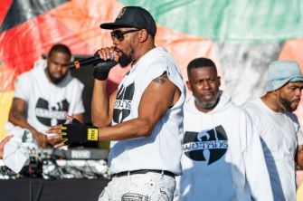 A performer rapping on stage with members of Wu-Tang Clan in the background.