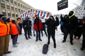 A group of protesters gathers in the snow, holding signs in support of Black Lives Matter and opposing police actions.