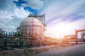 Industrial oil and gas facility with pipelines and storage tanks under a cloudy sky.