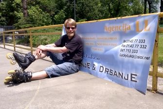 Former Slovenian Olympic figure skater Luka Klasinc sitting on skates beside a promotional banner.