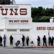 A line of people waiting outside a gun store, with signs indicating that they buy guns and collectibles. A line of people waiting outside a gun store, with signs indicating that they buy guns and collectibles.