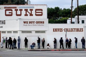 A line of people waiting outside a gun store, with signs indicating that they buy guns and collectibles.