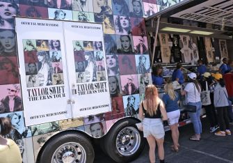 Fans line up at a merchandise truck for Taylor Swift's Eras Tour, showcasing various items associated with the concert.