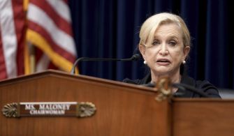 Democratic Representative Carolyn Maloney speaking at a congressional hearing, with an American flag in the background.