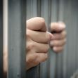 Close-up of hands gripping prison bars, symbolizing confinement and legal issues. Close-up of hands gripping prison bars, symbolizing confinement and legal issues.