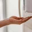 A hand receiving a squirt of hand sanitizer from a wall-mounted dispenser. A hand receiving a squirt of hand sanitizer from a wall-mounted dispenser.