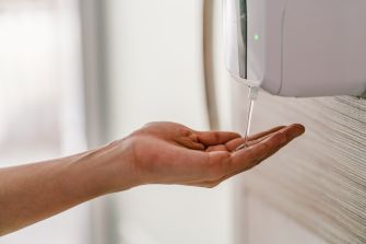 A hand receiving a squirt of hand sanitizer from a wall-mounted dispenser.