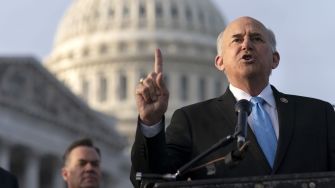 Republican Congressman Louie Gohmert speaking at a podium outside the U.S. Capitol, raising a finger to emphasize his point.