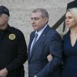 Two individuals, flanked by a police officer, leaving a courtroom following a hearing related to fraud charges. Two individuals, flanked by a police officer, leaving a courtroom following a hearing related to fraud charges.