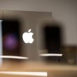 Apple logo displayed in a store with silhouettes of smartphones in the foreground. Apple logo displayed in a store with silhouettes of smartphones in the foreground.