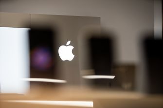 Apple logo displayed in a store with silhouettes of smartphones in the foreground.