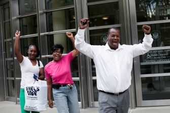 Group of people celebrating outside a building, raising their fists in solidarity and joy.
