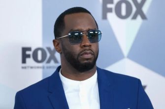 Sean "Diddy" Combs at a public event, wearing sunglasses and a blue suit.
