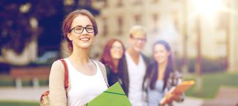 A group of college students smiling and walking on campus, holding school supplies.