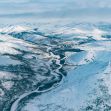 Aerial view of a snow-covered landscape in Alaska, featuring mountains and a winding river in the Arctic National Wildlife Refuge. Aerial view of a snow-covered landscape in Alaska, featuring mountains and a winding river in the Arctic National Wildlife Refuge.