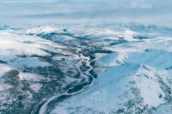 Aerial view of a snow-covered landscape in Alaska, featuring mountains and a winding river in the Arctic National Wildlife Refuge.