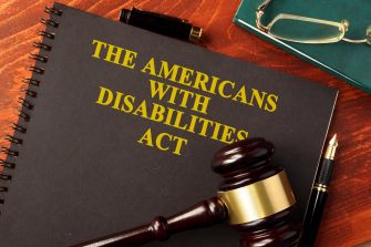 A gavel and a notebook with the title "The Americans with Disabilities Act" on a wooden surface, accompanied by a pen and glasses.